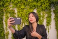 Young happy and beautiful Asian Chinese woman enjoying outdoors taking selfie with mobile phone at village garden playful and Royalty Free Stock Photo