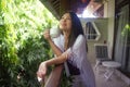 Young happy and beautiful Asian Chinese woman having morning coffee or tea at hotel terrace or home balcony leaning on the Royalty Free Stock Photo