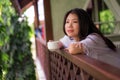 Young happy and beautiful Asian Chinese woman having morning coffee or tea at hotel terrace or home balcony leaning on the Royalty Free Stock Photo