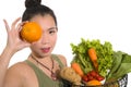 Young happy and beautiful Asian Chinese woman holding basket full of vegetables smiling cheerful holding orange playful in healthy