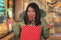 Young happy and beautiful Asian Chinese woman holding red shopping bag buying Christmas present in city mall smiling excited and Royalty Free Stock Photo