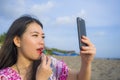 Young happy and beautiful Asian Chinese woman retouching her makeup applying red lipstick on her lips using mobile phone as mirror Royalty Free Stock Photo