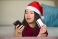 Young happy and beautiful Asian Chinese woman in Santa Claus hat holding credit card using mobile phone for Christmas online shopp Royalty Free Stock Photo