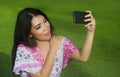 Young happy and beautiful Asian Chinese woman taking selfie pic with mobile phone camera posing sensual and playful outdoors on gr Royalty Free Stock Photo