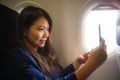 Young happy and beautiful Asian Chinese woman traveling for business inside airplane cabin smiling cheerful using mobile phone Royalty Free Stock Photo