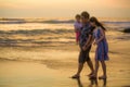 Young happy and beautiful Asian Japanese couple holding baby girl daughter walking on sunset beach enjoying together romantic Royalty Free Stock Photo