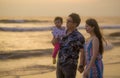 Young happy and beautiful Asian Korean couple holding baby girl daughter walking on sunset beach enjoying together romantic summer Royalty Free Stock Photo