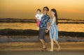 Young happy and beautiful Asian Korean couple holding baby girl daughter walking on sunset beach enjoying together romantic summer Royalty Free Stock Photo