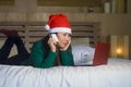 Young happy and beautiful Asian Korean girl on bed in Santa Christmas hat using credit card and laptop computer for online shoppin Royalty Free Stock Photo