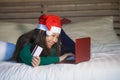 Young happy and beautiful Asian Korean girl on bed in Santa Christmas hat using credit card and laptop computer for online shoppin Royalty Free Stock Photo