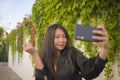 Young happy and beautiful Asian Korean woman enjoying outdoors taking selfie with mobile phone at village garden playful and Royalty Free Stock Photo
