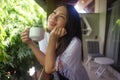 Young happy and beautiful Asian Korean woman having morning coffee or tea at hotel terrace or home balcony leaning on the Royalty Free Stock Photo