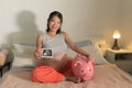 Young happy and beautiful Asian Korean woman holding ultrasound and piggy bank sitting on bed pregnant smiling cheerful caring for Royalty Free Stock Photo