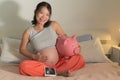 Young happy and beautiful Asian Korean woman holding ultrasound and piggy bank sitting on bed pregnant smiling cheerful caring for Royalty Free Stock Photo