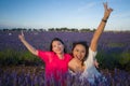 Young happy and beautiful Asian korean woman playing on lavender flowers field with her hispanic girlfriend enjoying sweet