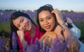 Young happy and beautiful Asian korean woman playing on lavender flowers field with her hispanic girlfriend enjoying sweet