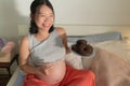 Young happy and beautiful Asian Korean woman pregnant sitting on bed holding dish full of chocolate donuts craving for sweet food Royalty Free Stock Photo