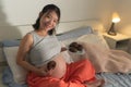 Young happy and beautiful Asian Korean woman pregnant sitting on bed holding dish full of chocolate donuts craving for sweet food Royalty Free Stock Photo