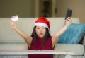 Young happy and beautiful Asian Korean woman in Santa Claus hat holding credit card using mobile phone for Christmas online shoppi Royalty Free Stock Photo