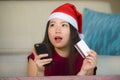 Young happy and beautiful Asian Korean woman in Santa Claus hat holding credit card using mobile phone for Christmas online shoppi Royalty Free Stock Photo