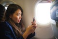 Young happy and beautiful Asian Korean woman traveling for business inside airplane cabin smiling cheerful using mobile phone in Royalty Free Stock Photo