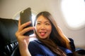 Young happy and beautiful Asian Korean woman traveling for business inside airplane cabin smiling cheerful using mobile phone Royalty Free Stock Photo