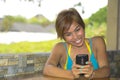 Young happy beautiful and attractive Asian woman sitting in coffee shop using internet app on mobile phone laughing excited outdoo Royalty Free Stock Photo