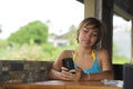 Young happy beautiful and attractive Asian woman sitting in coffee shop using internet app on mobile phone smiling relaxed outdoor Royalty Free Stock Photo