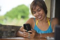 Young happy beautiful and attractive Asian woman sitting in coffee shop using internet app on mobile phone smiling relaxed outdoor Royalty Free Stock Photo