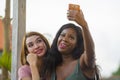 Young happy and beautiful black afro American woman enjoying holidays at tropical resort with Asian girlfriend taking selfie