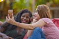 Young happy and beautiful black afro American woman enjoying holidays at tropical resort with Asian girlfriend taking selfie