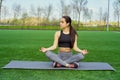 Young happy and beautiful brunette girl doing yoga workout in park, sitting in lotus pose meditating enjoying retreat in balance a Royalty Free Stock Photo