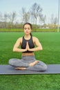 Young happy and beautiful brunette girl doing yoga workout in park, sitting in lotus pose meditating enjoying retreat in balance a Royalty Free Stock Photo