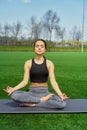 Young happy and beautiful brunette girl doing yoga workout in park, sitting in lotus pose meditating enjoying retreat in balance a Royalty Free Stock Photo