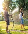 Young happy beautiful couple hosing in the garden, summer happiness and love concept, poured water from a garden hose of a spray Royalty Free Stock Photo