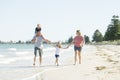 Young happy and beautiful family mother father holding hand of son and daughter walking joyful on the beach enjoying Summer holida Royalty Free Stock Photo