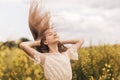 Young beautiful girl with long hair flying in the wind against the background of rapeseed field. Breeze playing with girl`s hair