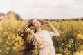 Young beautiful girl with long hair flying in the wind against the background of rapeseed field. Breeze playing with girl`s hair