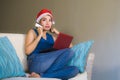 Young happy and beautiful girl relaxed at home couch in Santa hat using laptop computer paying for Christmas present with credit c Royalty Free Stock Photo