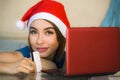Young happy and beautiful girl relaxed at home couch in Santa hat using laptop computer paying for Christmas present with credit c Royalty Free Stock Photo