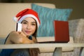 Young happy and beautiful girl relaxed at home couch in Santa hat using laptop computer paying for Christmas present with credit c Royalty Free Stock Photo