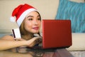 Young happy and beautiful girl relaxed at home couch in Santa hat using laptop computer paying for Christmas present with credit c Royalty Free Stock Photo