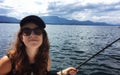 A young happy beautiful hipster girl holding a fishing rod fishing in the ocean on a small boat in the gulf islands