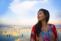 Young happy and beautiful Korean woman in traditional Asian dress at sunrise sea landscape looking away thoughtful and pensive in Royalty Free Stock Photo