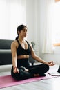 Young happy beautiful woman practicing yoga at home sitting in lotus pose on yoga mat meditating smiling relaxed Royalty Free Stock Photo