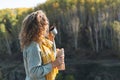 Young happy beautiful woman traveller with curly hair eating hot dog and drinking tea on view background of mountains and river, Royalty Free Stock Photo