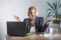 Young happy black afro american woman listening to music with headphones excited and joyful working at laptop computer desk at mod