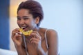 Young happy black woman sits in a bed and eating orange slice. Royalty Free Stock Photo