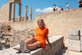 A young blonde woman is sitting and enjoying the view of the coast near the city of Lindos, Greece. Royalty Free Stock Photo