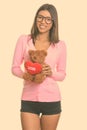 Young happy Brazilian nerd woman smiling while holding teddy bear with heart and love sign Royalty Free Stock Photo